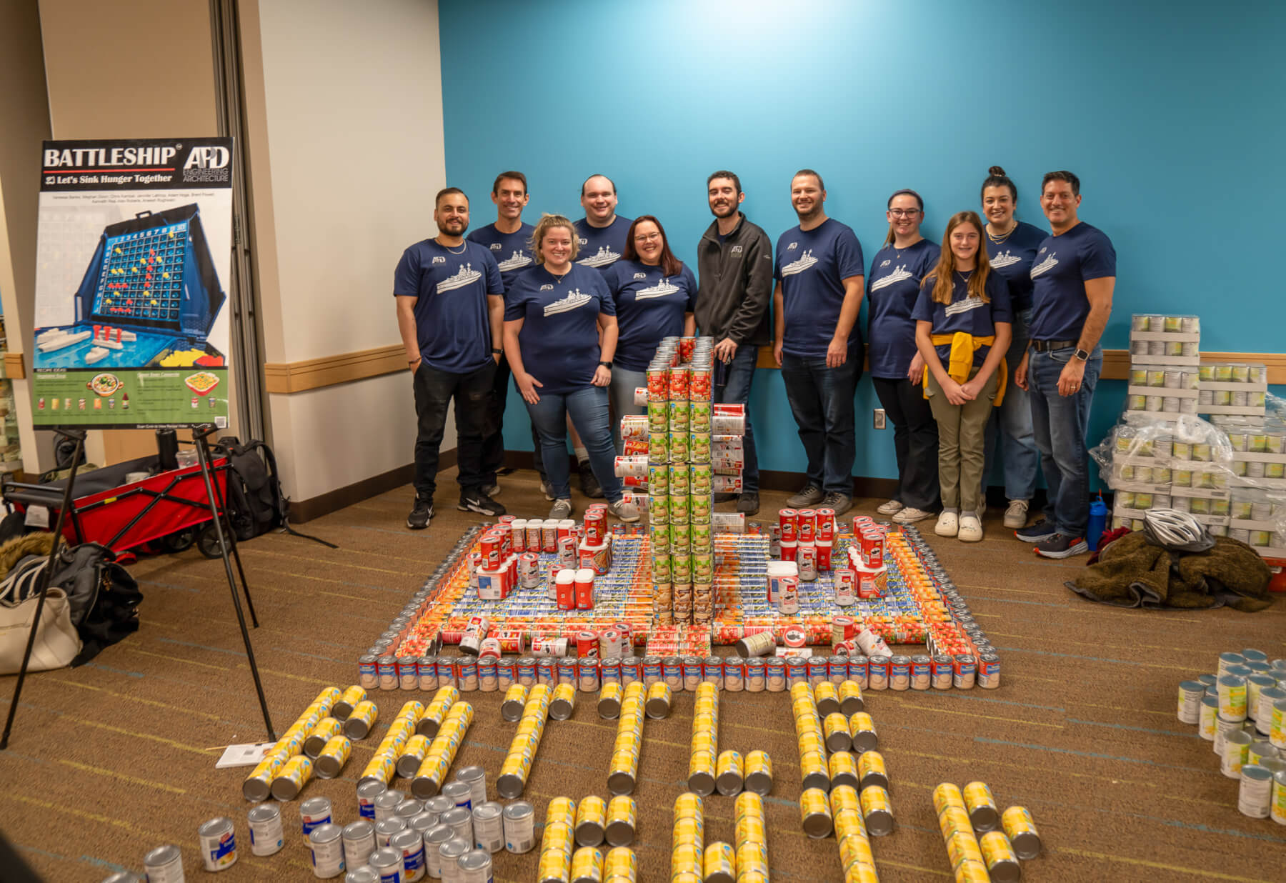 Food cans stacked to build a structure with eleven people behind the structure