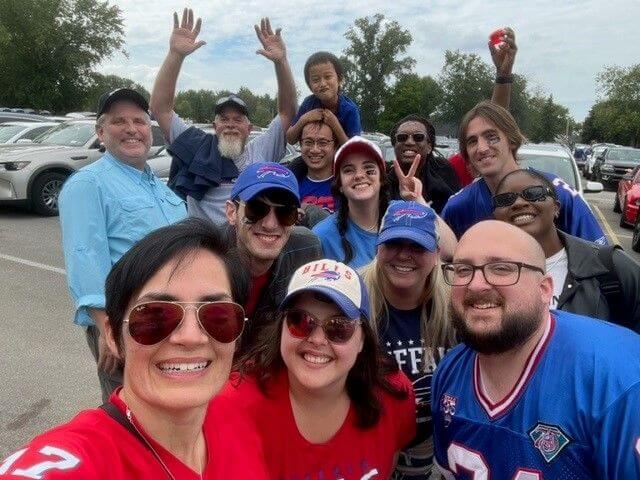 A selfie with thirteen people in a parking lot wearing Buffalo Bills apparel