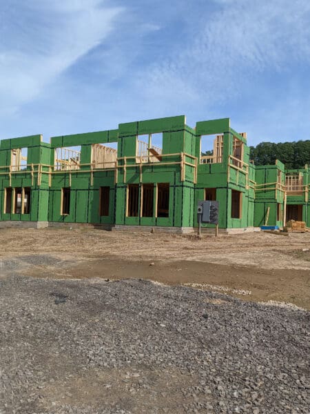 Construction site with green insulation panels on a building frame under a clear sky.