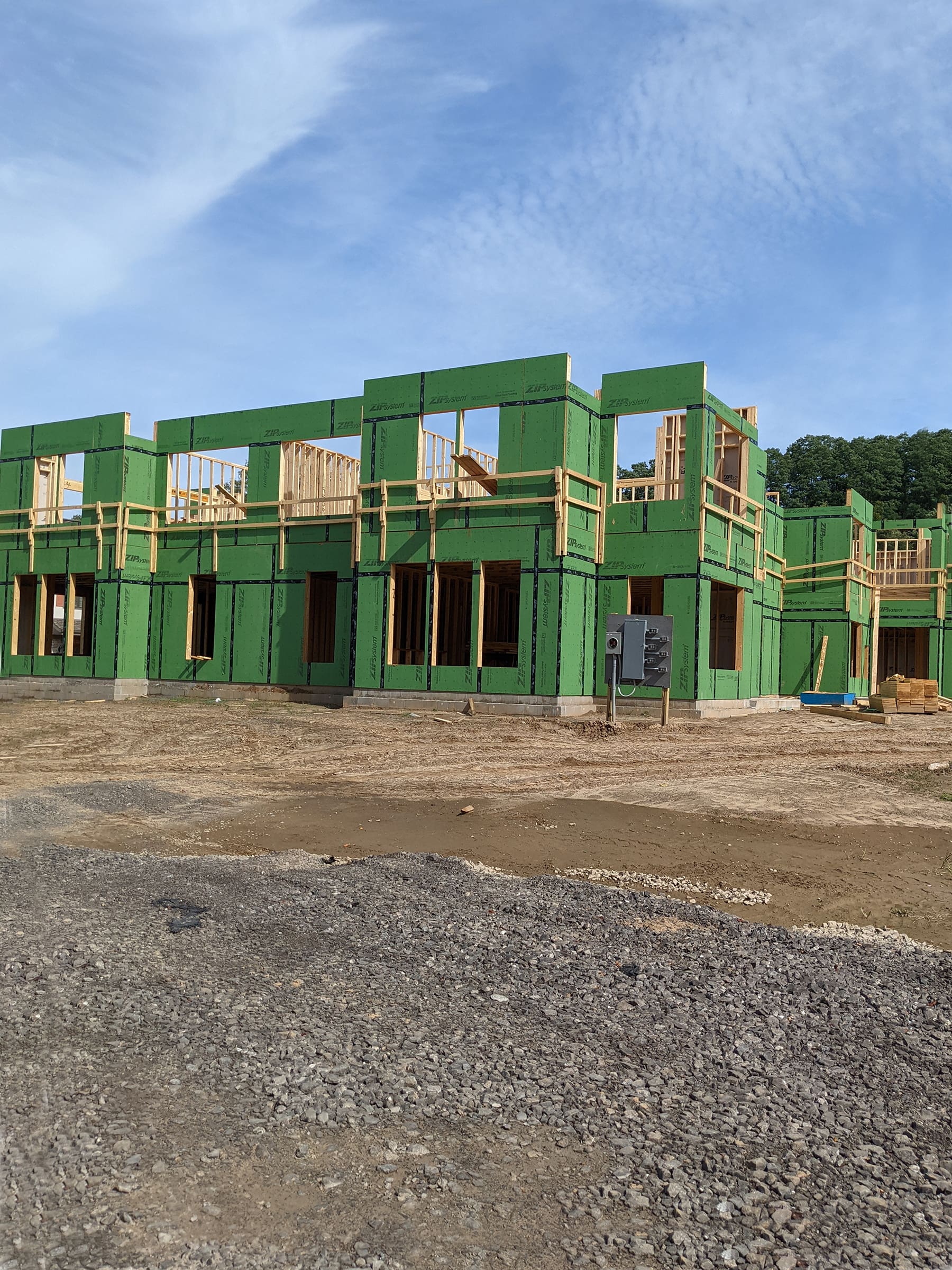 Construction site with green insulation panels on a building frame under a clear sky.