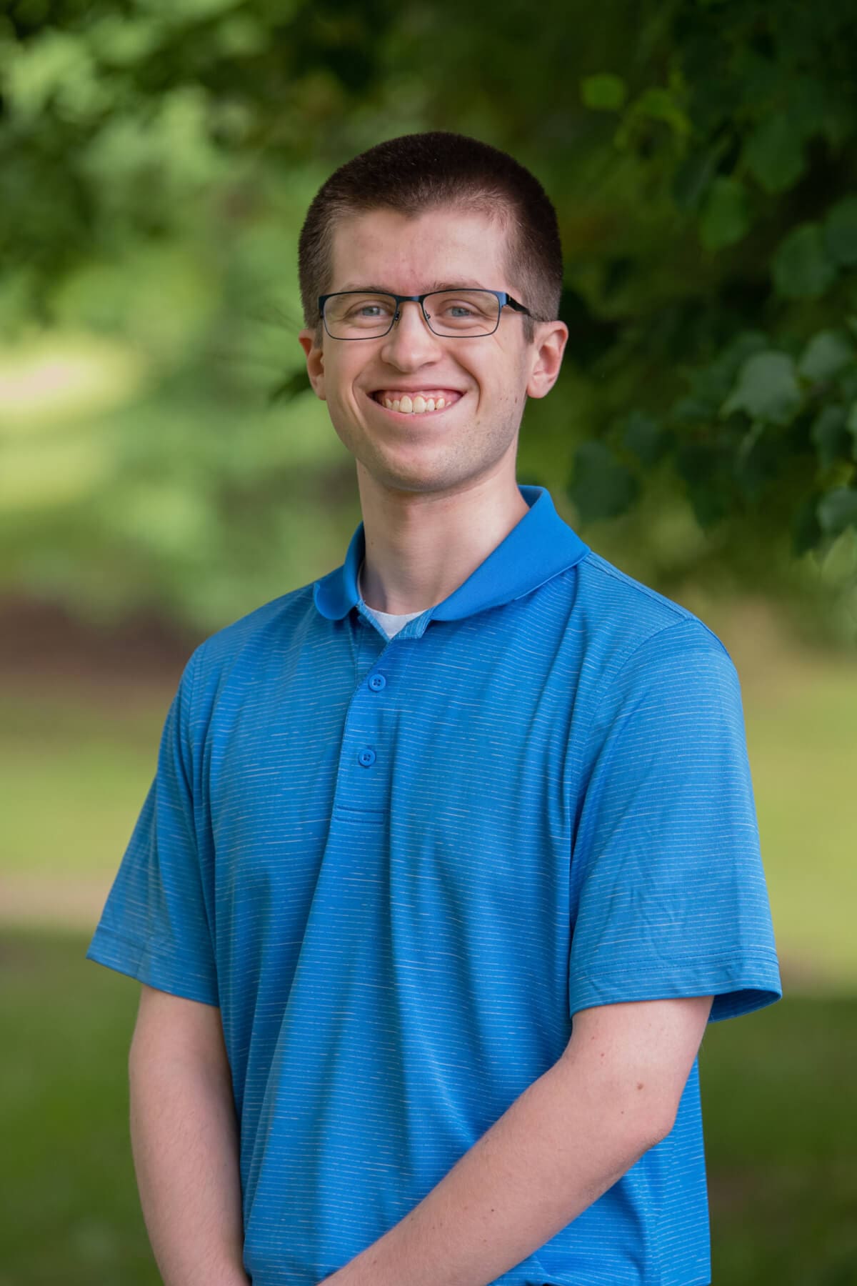 Professional headshot of man standing outdoors with a blurred green background.