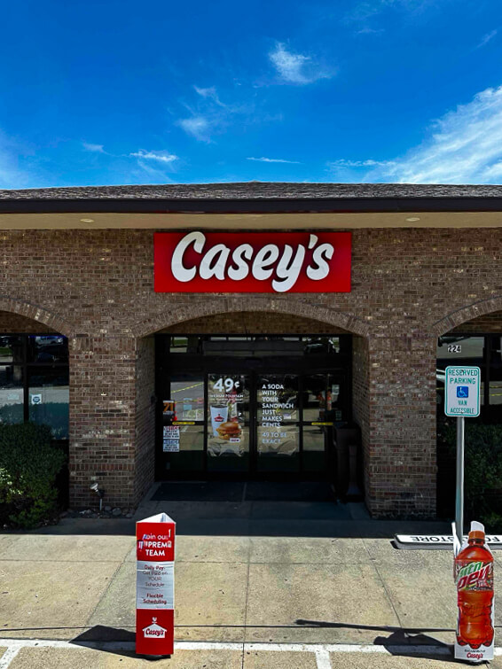 Entrance to a Casey's convenience store with promotional banners and signs for deals on food and drinks.