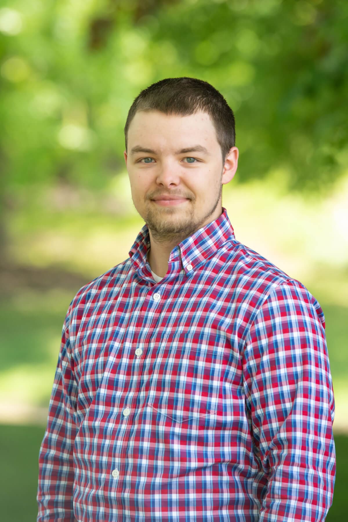 Professional headshot of man standing outdoors with a blurred green background.