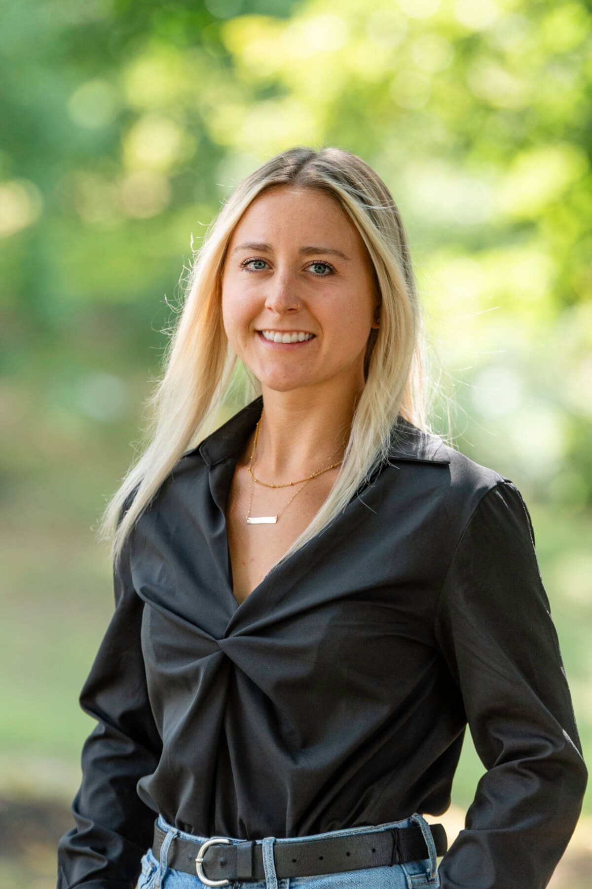 Professional headshot of woman standing outdoors with a blurred green background.