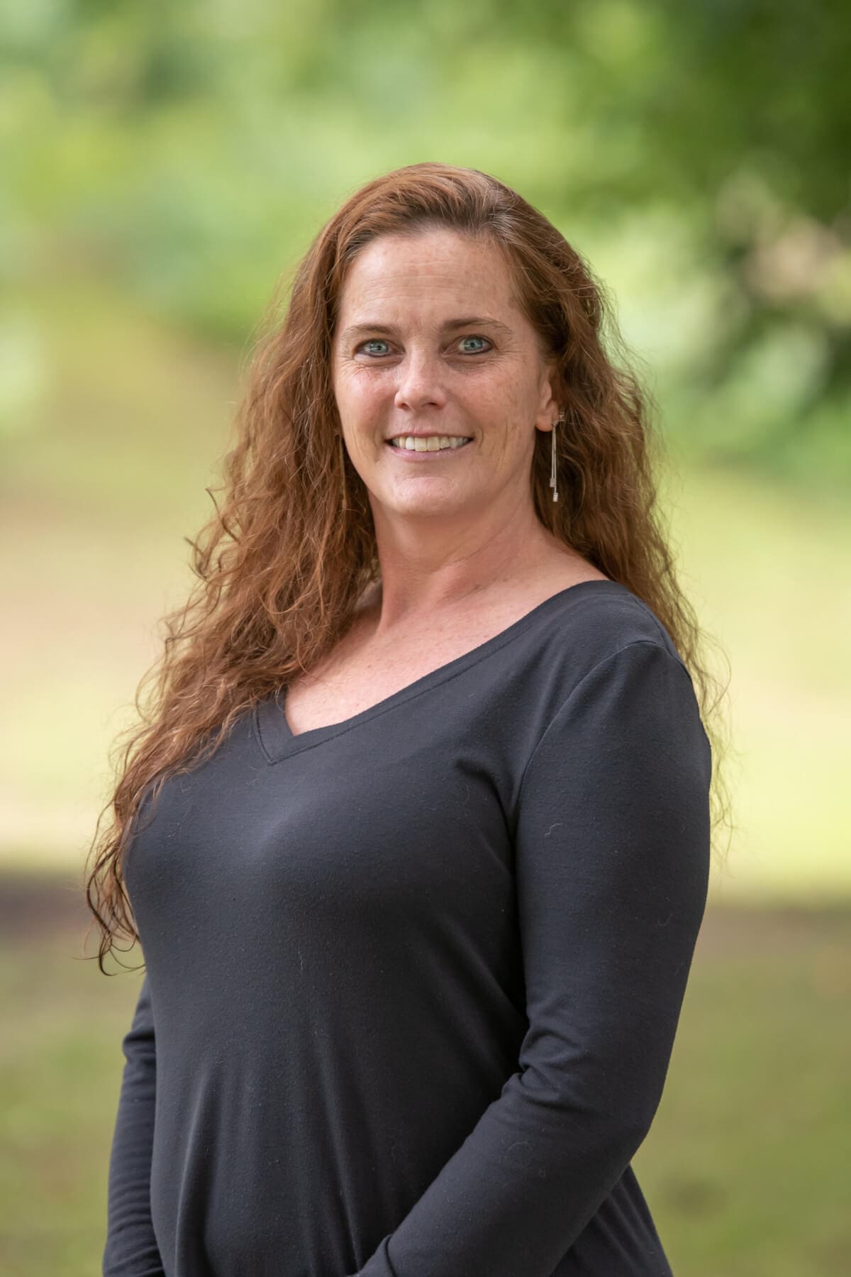 Professional headshot of man standing outdoors with a blurred green background.