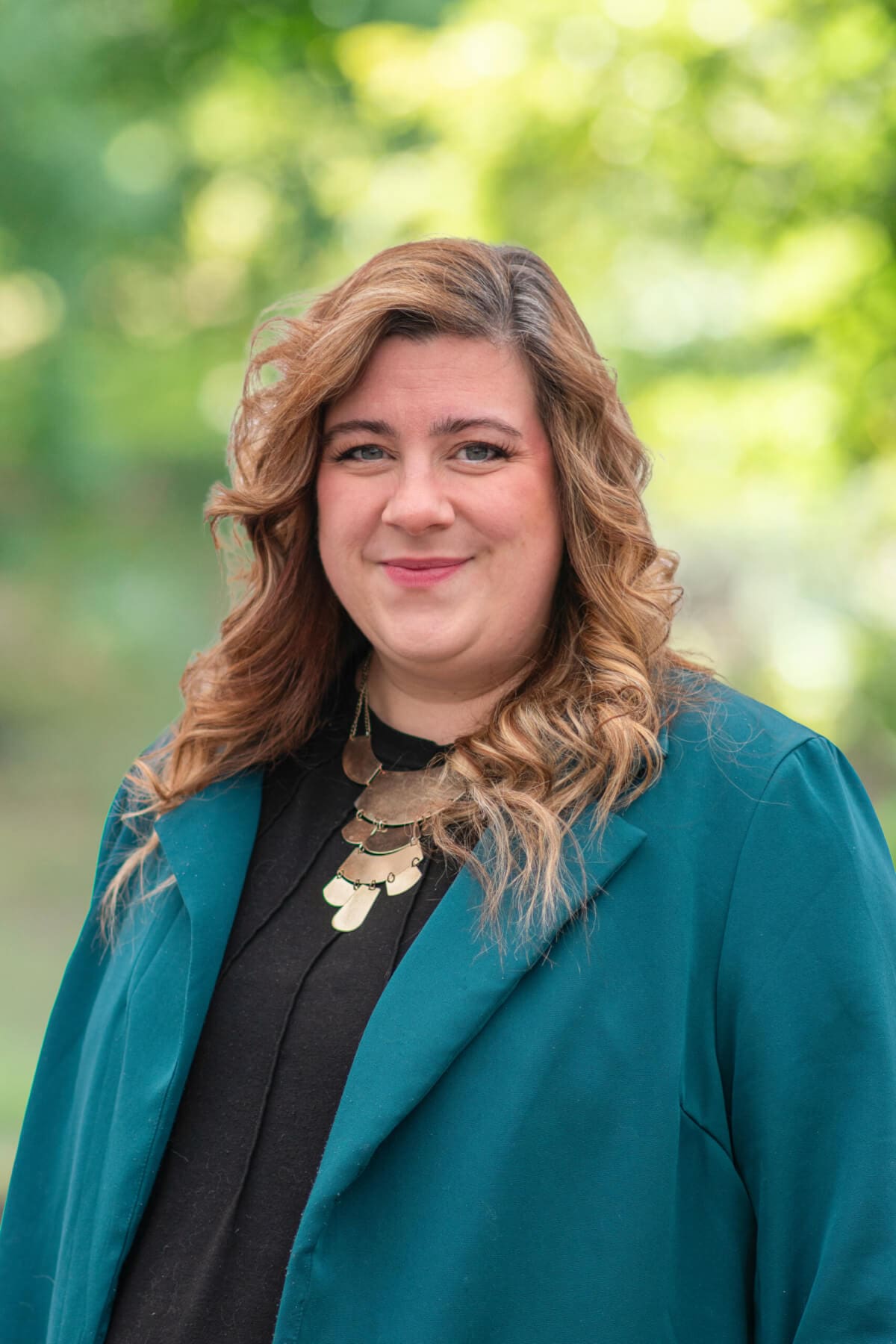 Professional headshot of man standing outdoors with a blurred green background.