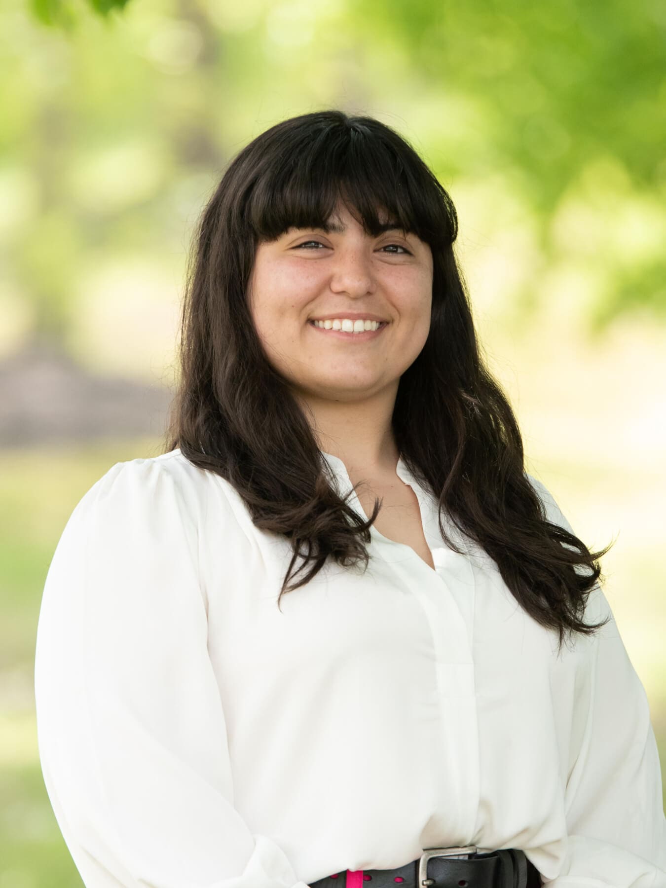 Professional headshot of woman standing outdoors with a blurred green background.