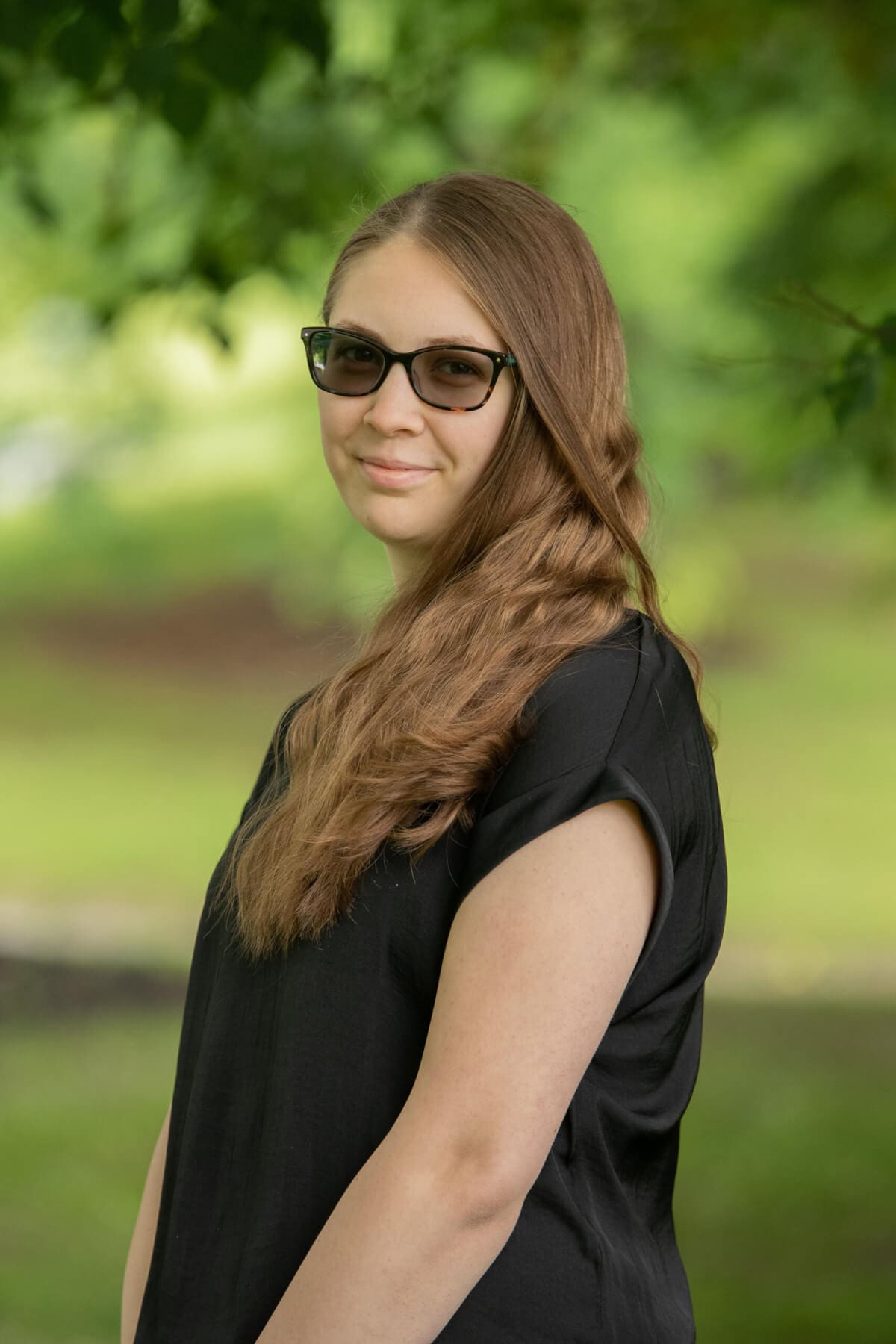Professional headshot of woman standing outdoors with a blurred green background.