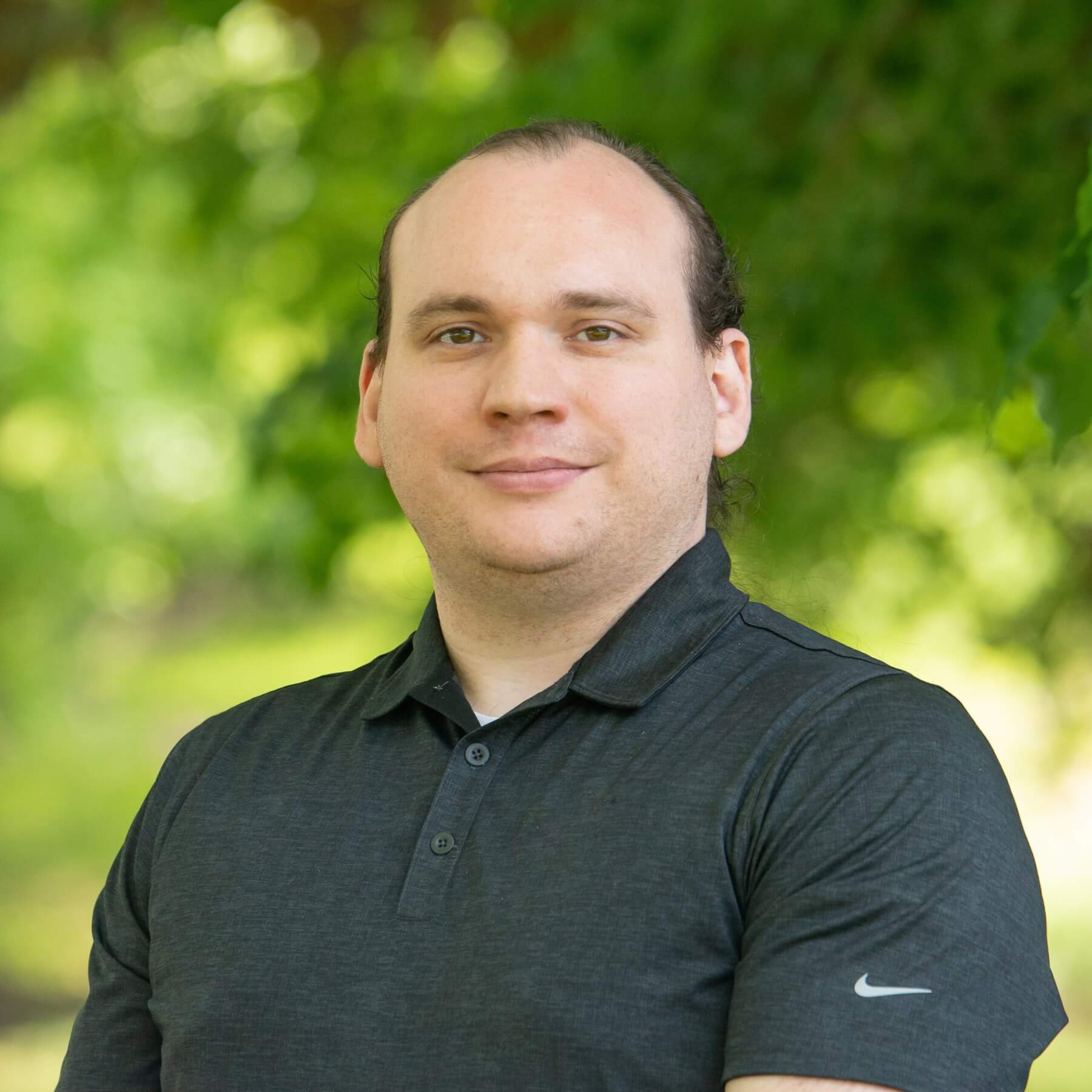 Professional headshot of man standing outdoors with a blurred green background.
