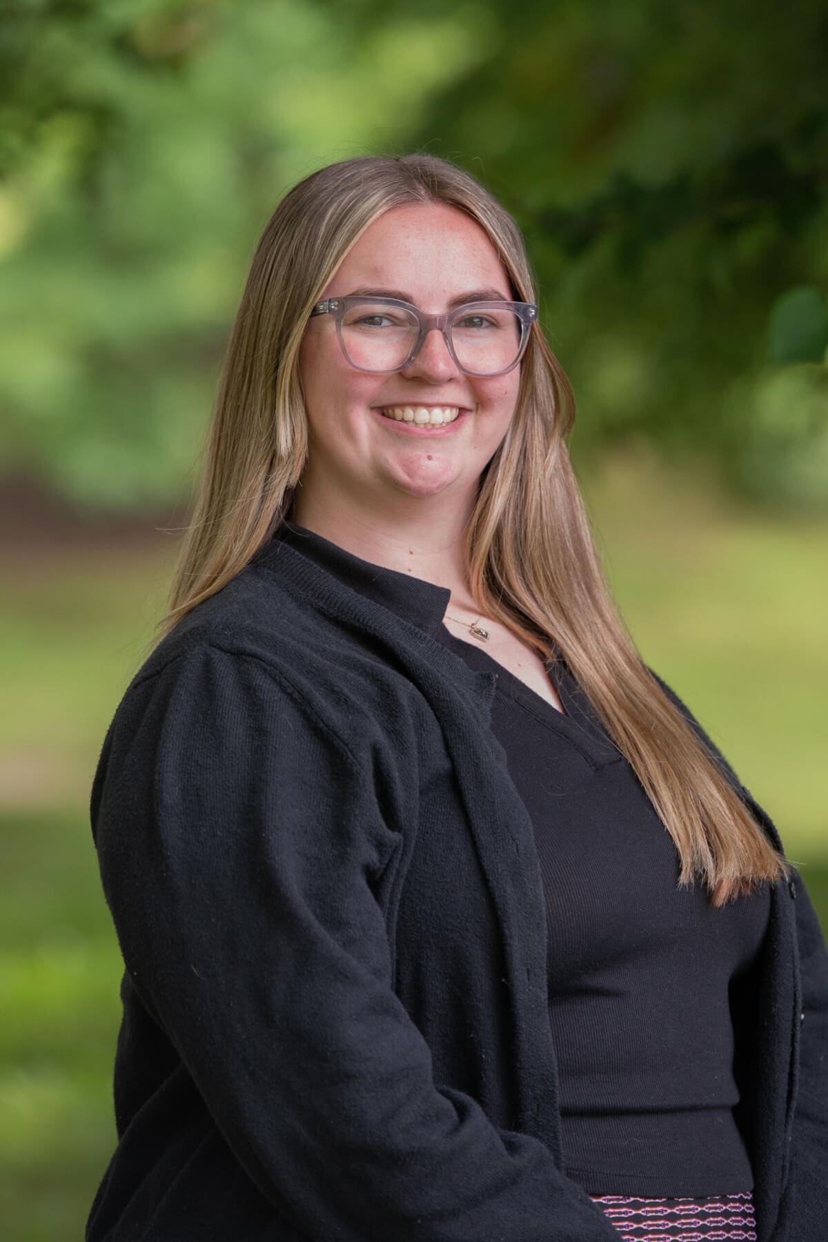 Professional headshot of woman standing outdoors with a blurred green background.