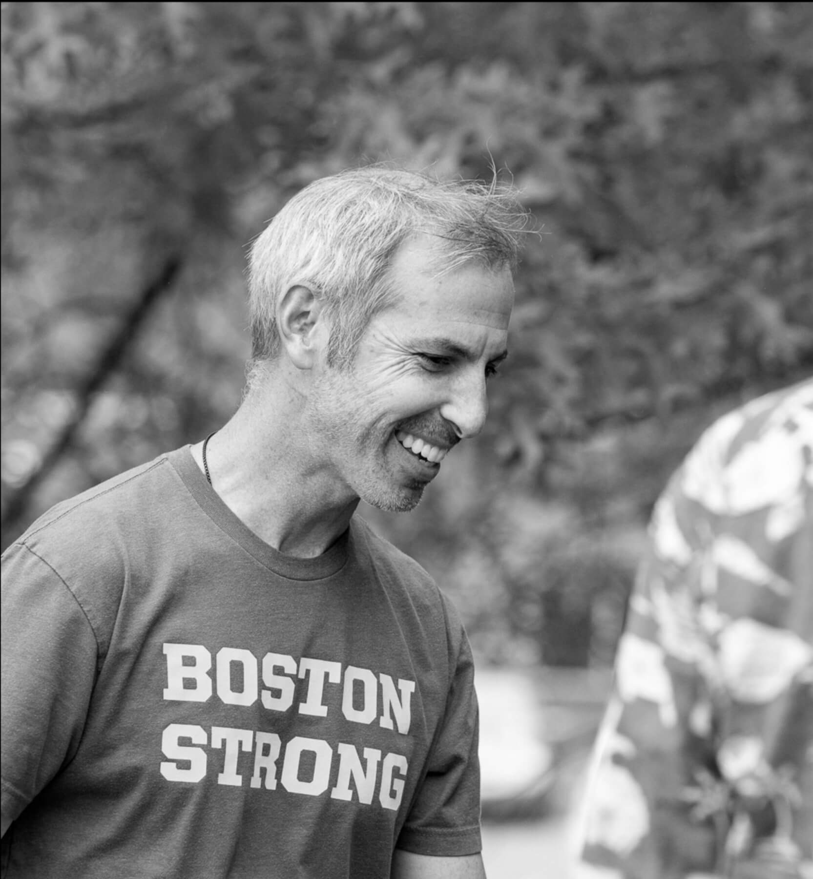 Man smiling in a Boston Strong shirt, outdoors.