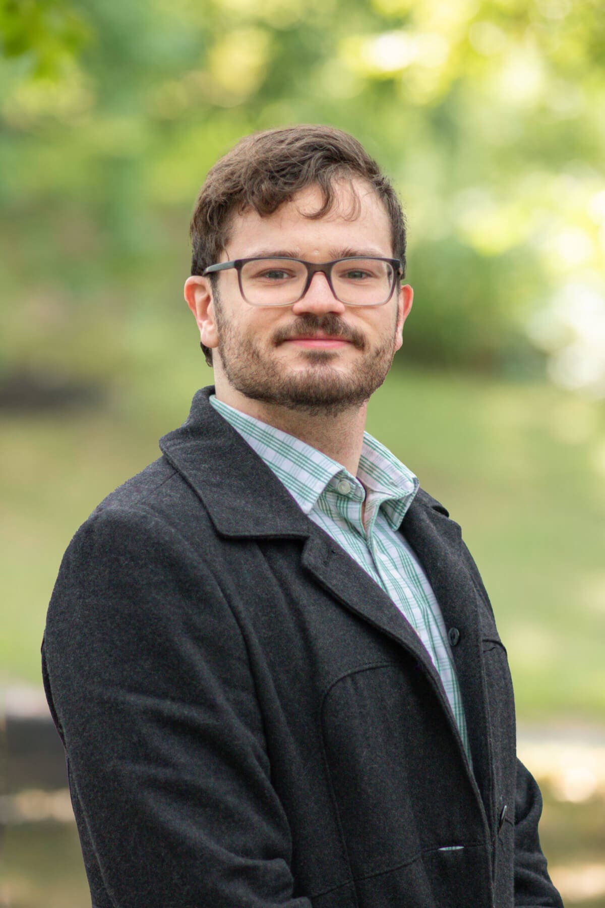 Professional headshot of man standing outdoors with a blurred green background.