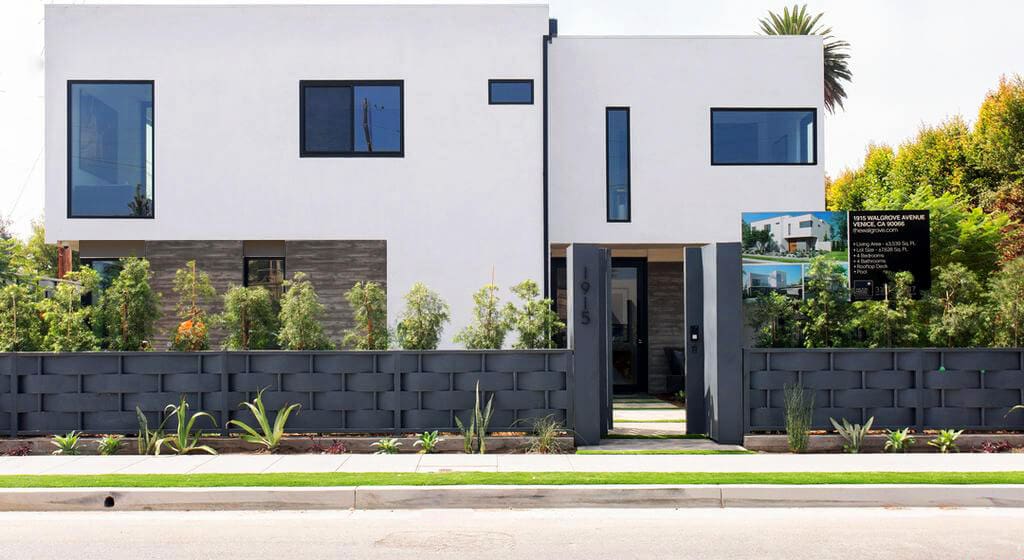 Modern white house exterior with large windows and a landscaped front yard. Luxurious real estate.