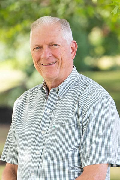 Professional headshot of man standing outdoors with a blurred green background.