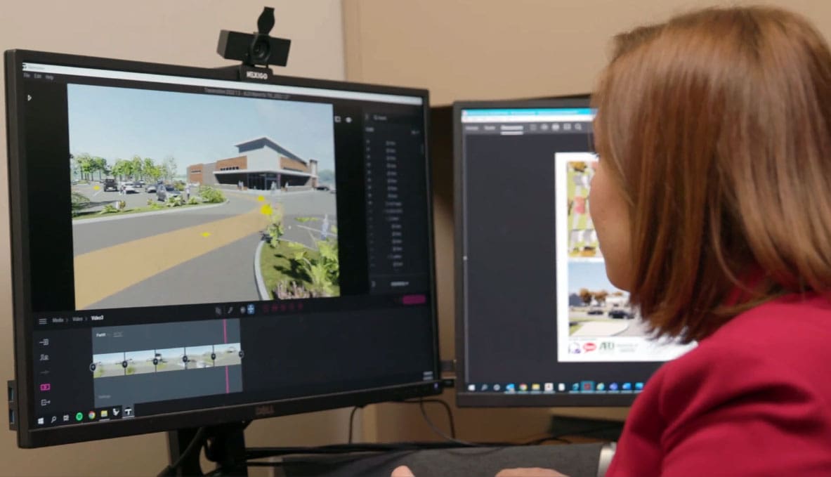 Person in red analyzing architectural design on dual monitors.