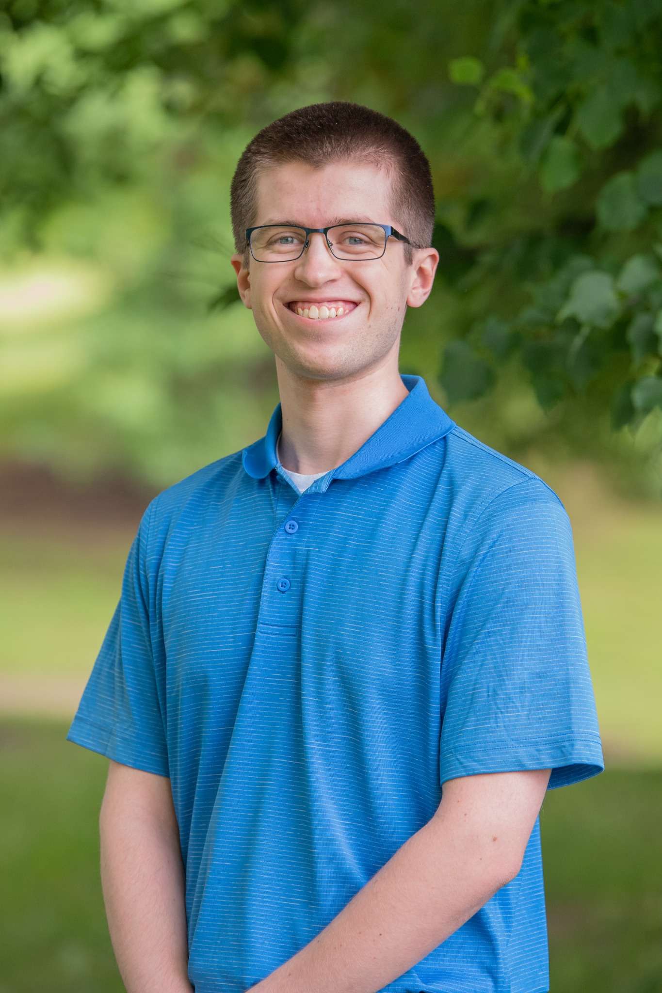 Professional headshot of man standing outdoors with a blurred green background.