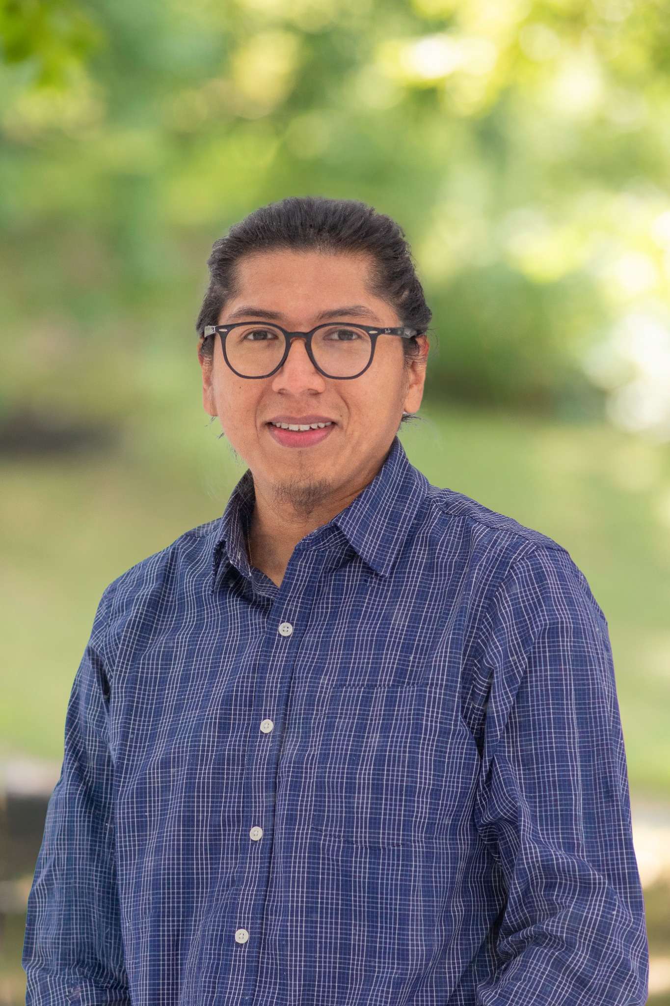 Professional headshot of man standing outdoors with a blurred green background.
