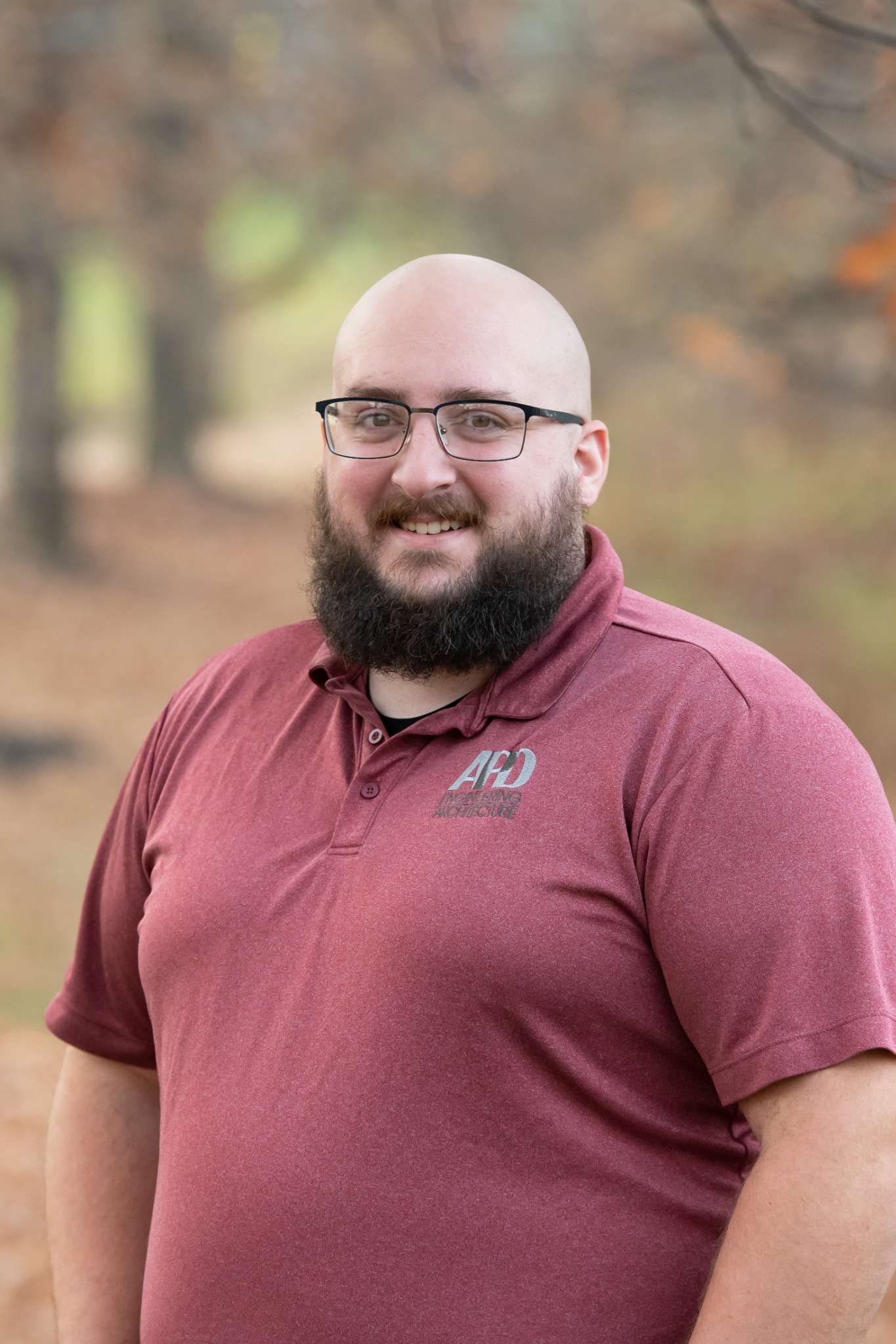 Professional headshot of man standing outdoors with a blurred green background.