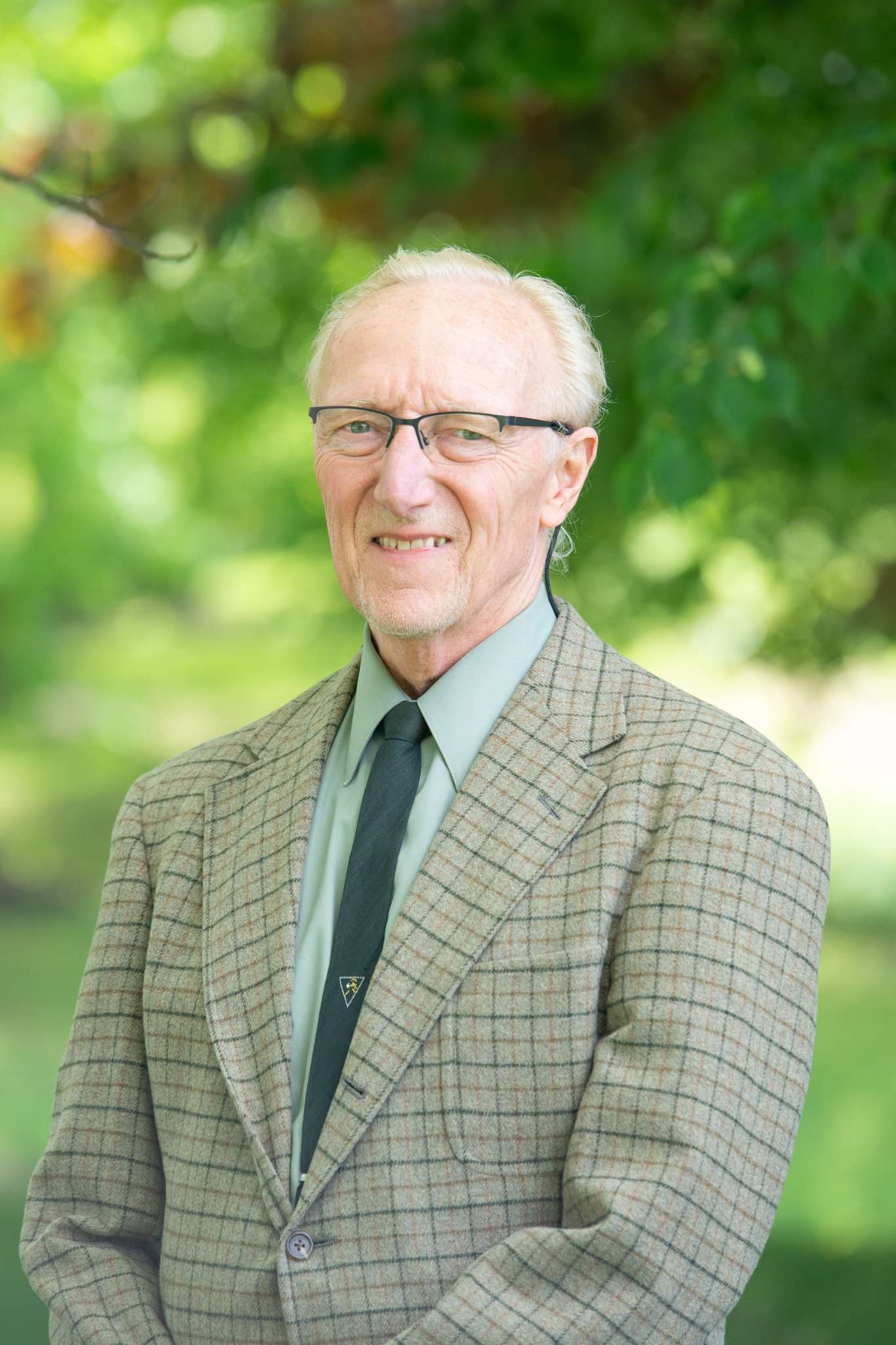 Professional headshot of man standing outdoors with a blurred green background.