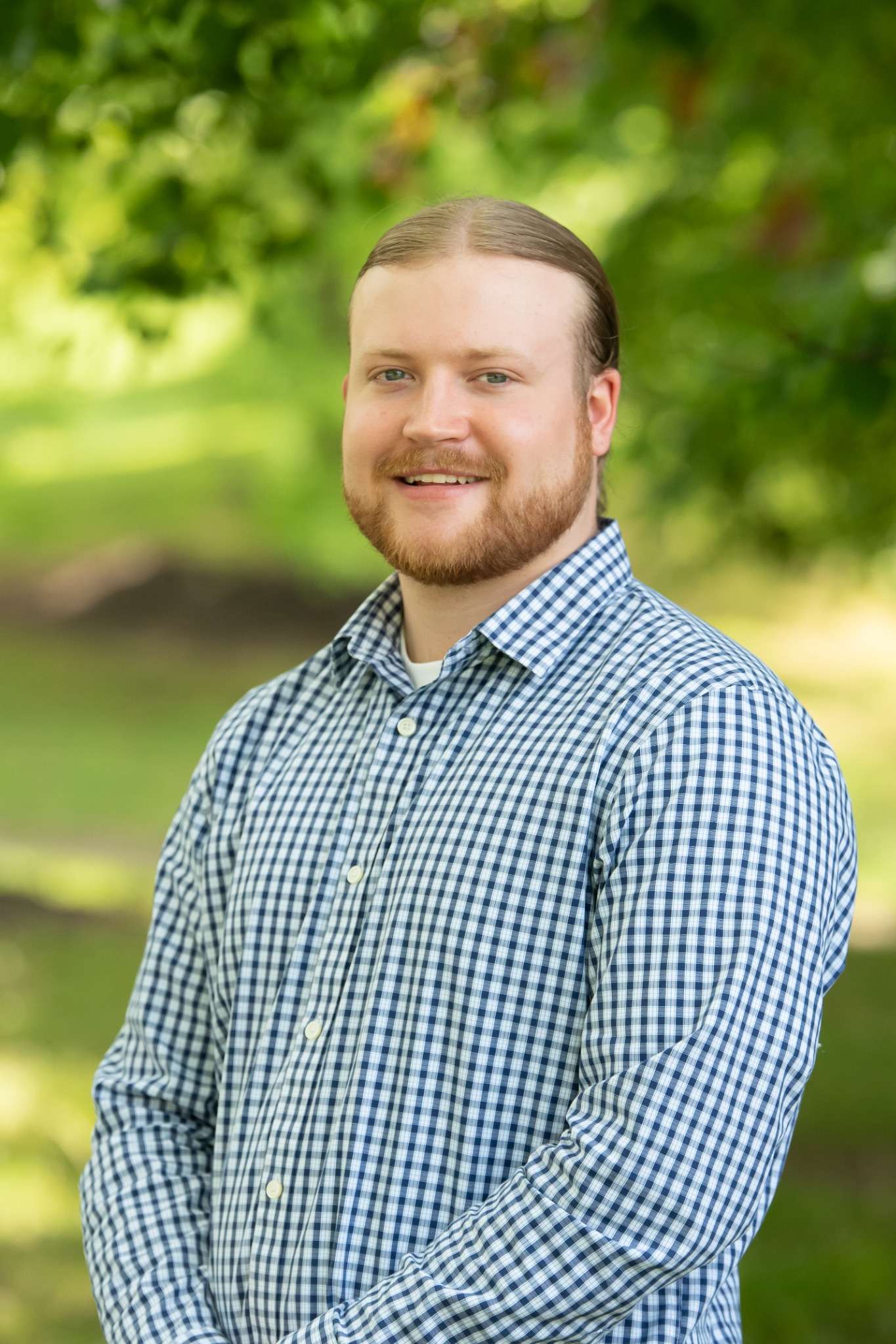 Professional headshot of man standing outdoors with a blurred green background.