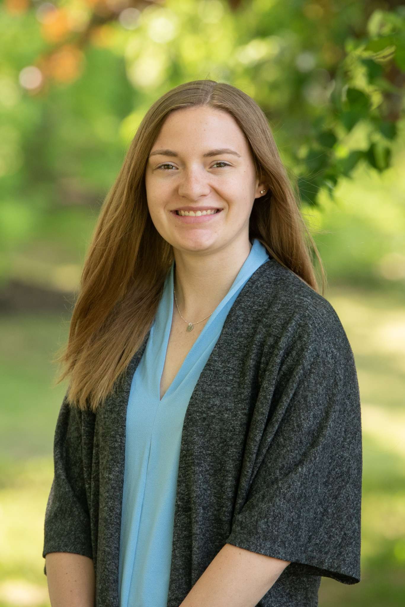 Professional headshot of woman standing outdoors with a blurred green background.