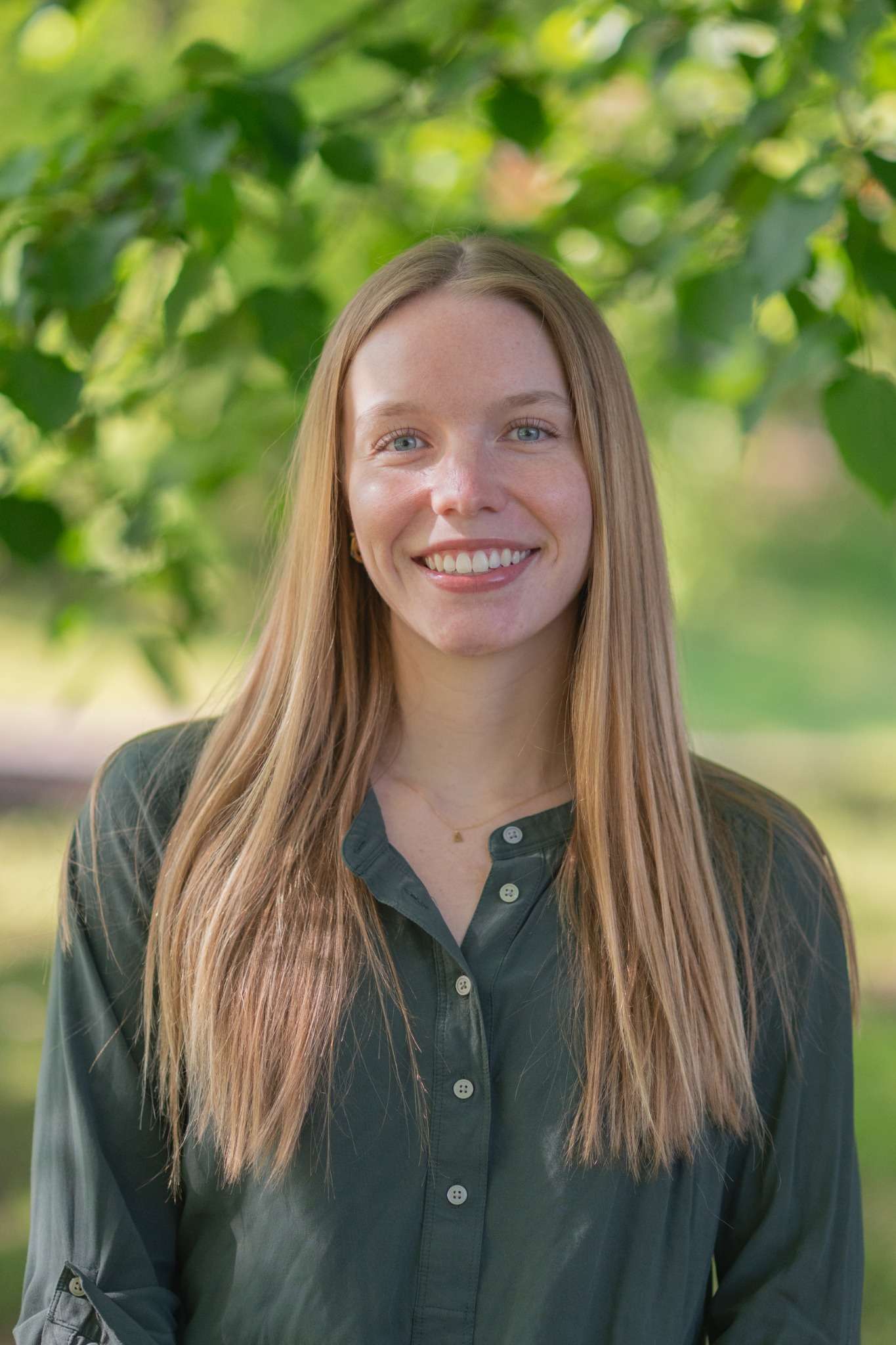Smiling woman outdoors, under leafy green trees. Ideal for nature-focused lifestyle content.