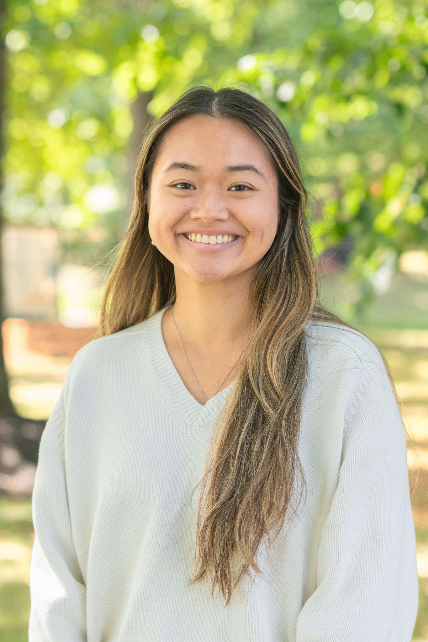 Professional headshot of woman standing outdoors with a blurred green background.