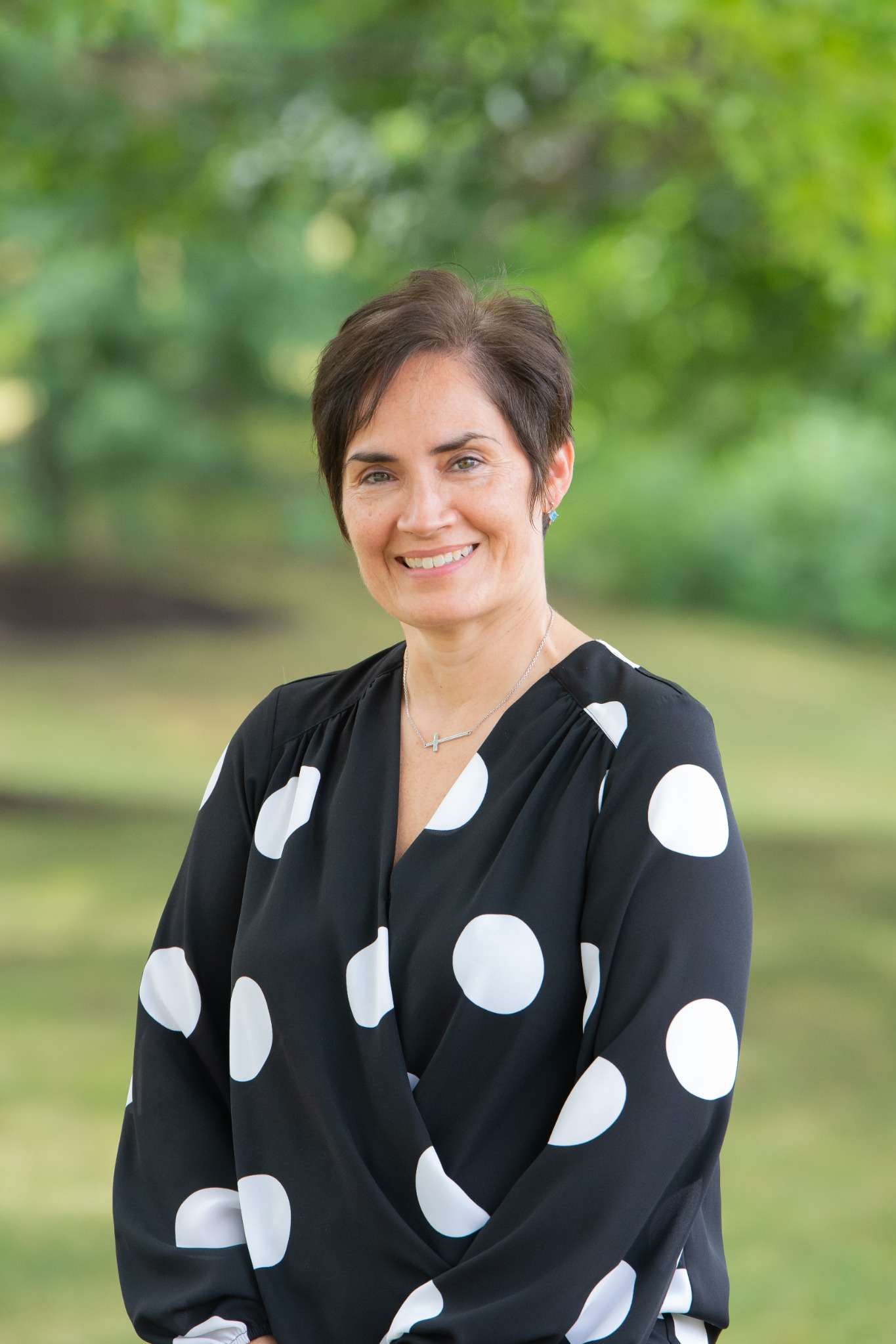 Professional headshot of woman standing outdoors with a blurred green background.