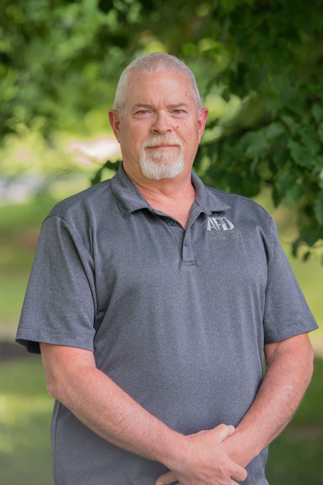 Professional headshot of man standing outdoors with a blurred green background.