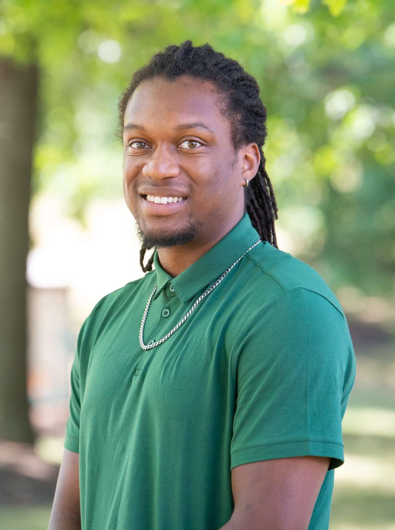 Professional headshot of man standing outdoors with a blurred green background.
