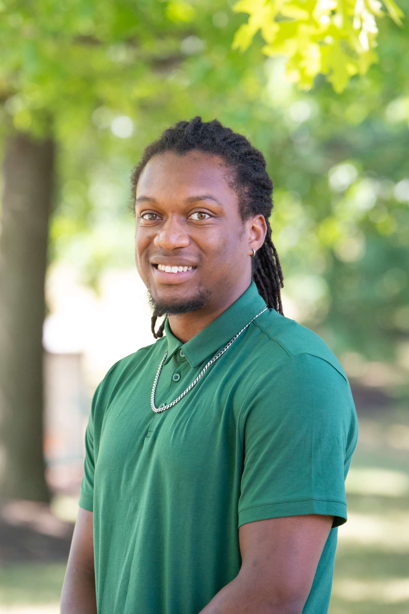 Professional headshot of man standing outdoors with a blurred green background.