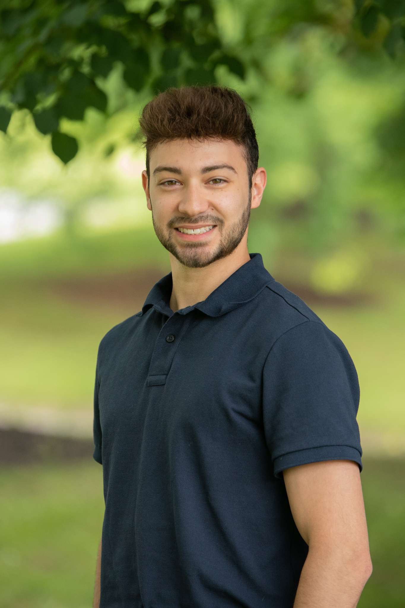 Professional headshot of man standing outdoors with a blurred green background.