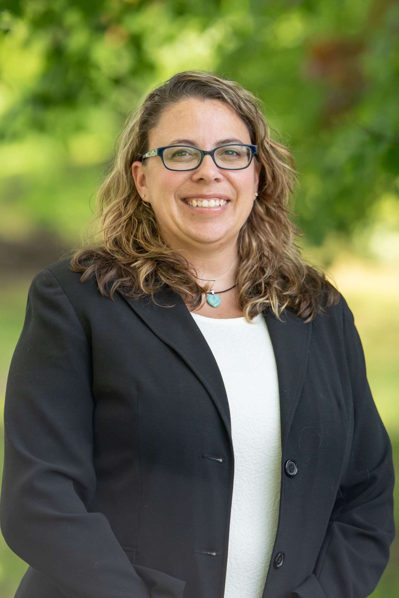 Professional headshot of woman standing outdoors with a blurred green background.
