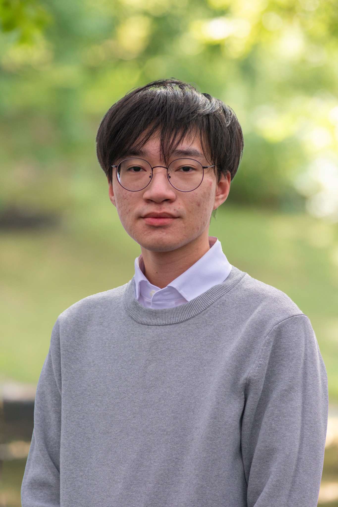 Professional headshot of man standing outdoors with a blurred green background.