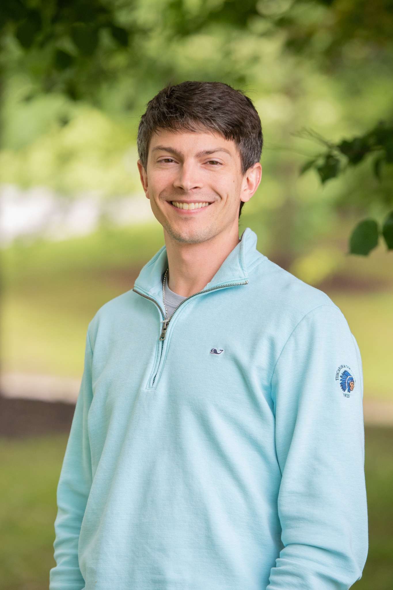Professional headshot of man standing outdoors with a blurred green background.