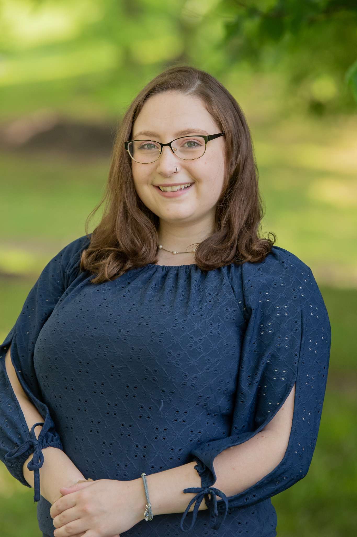 Professional headshot of woman standing outdoors with a blurred green background.