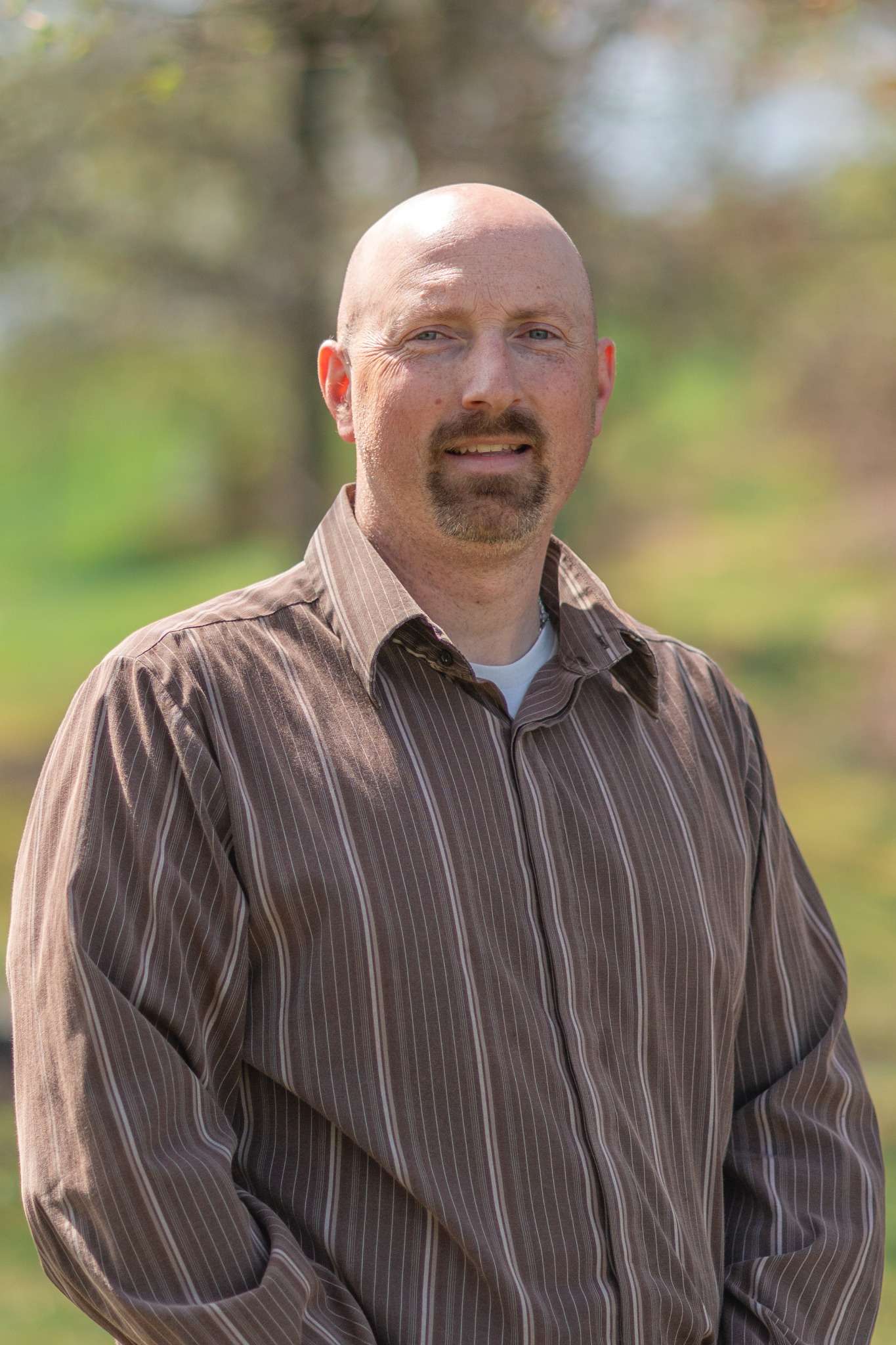 Professional headshot of man standing outdoors with a blurred green background.