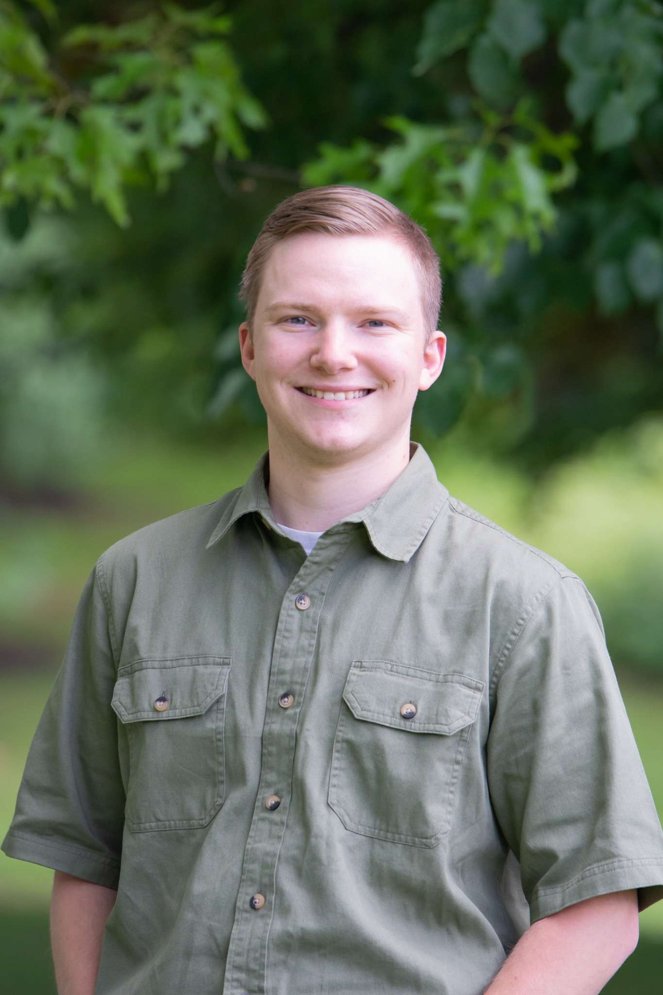 Professional headshot of man standing outdoors with a blurred green background.