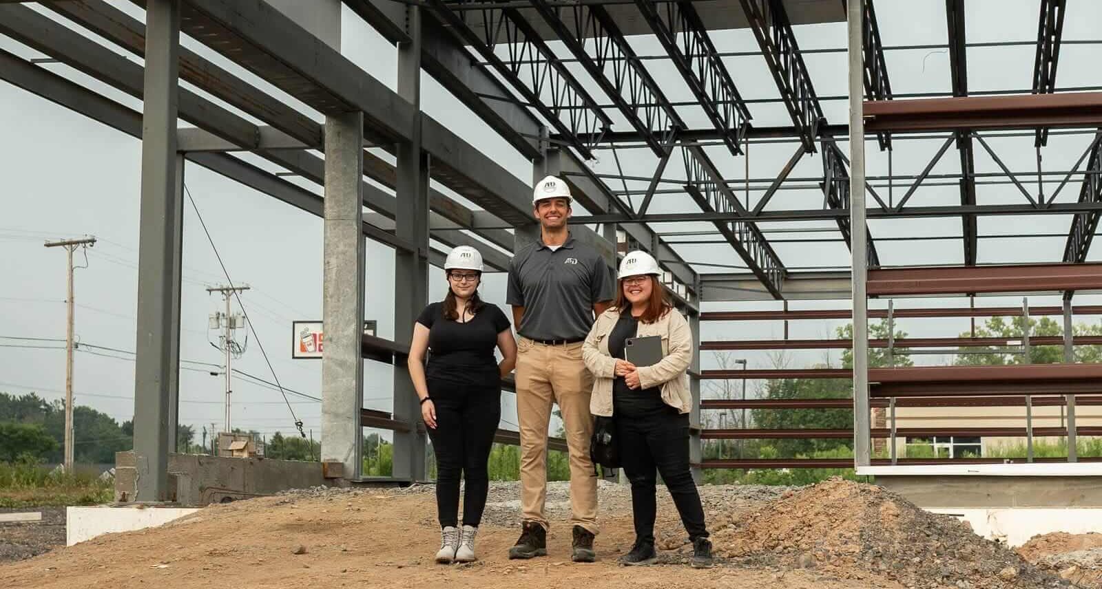 Construction team at a building site under steel framework, wearing hard hats.