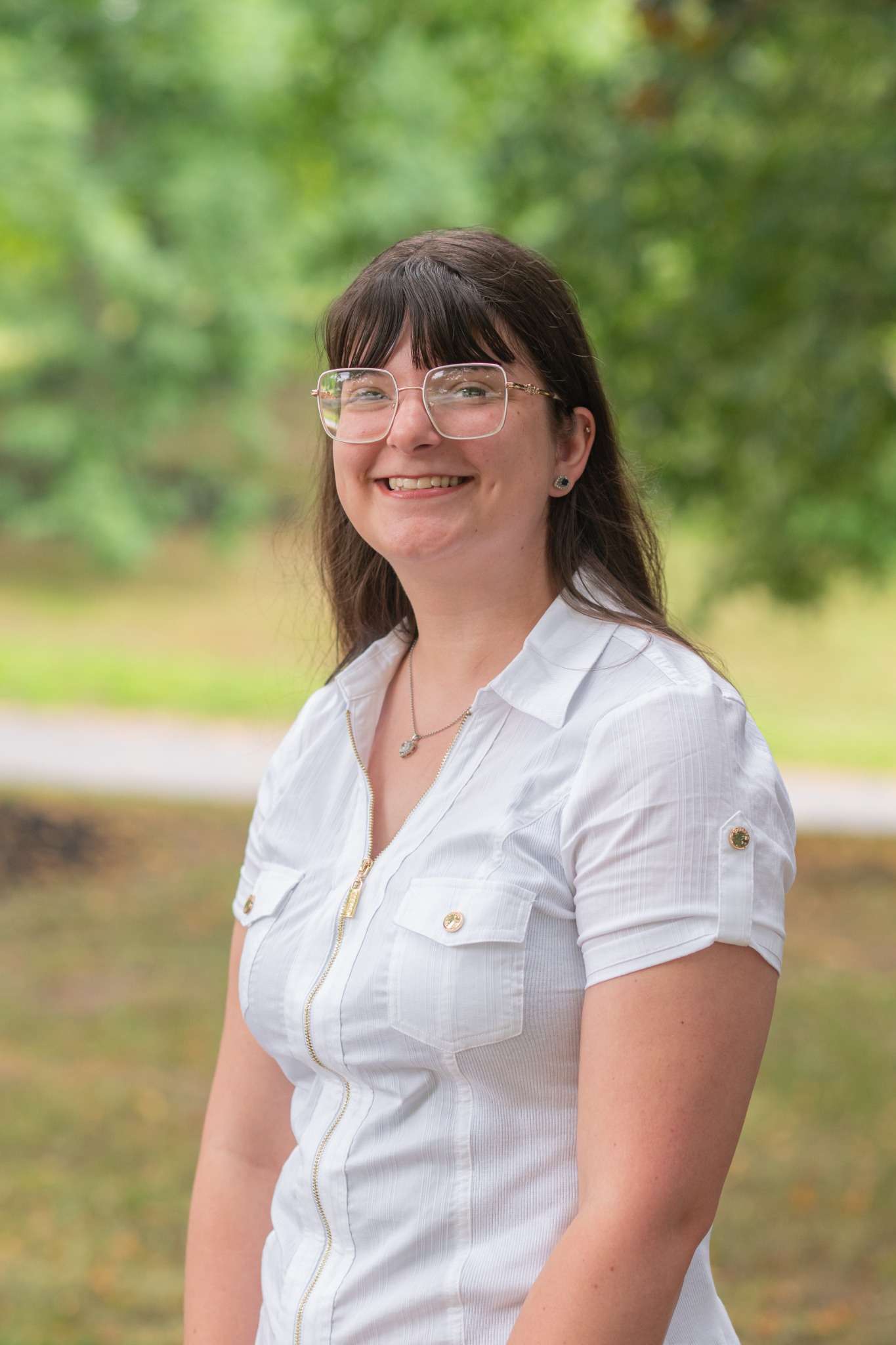 Professional headshot of woman standing outdoors with a blurred green background.
