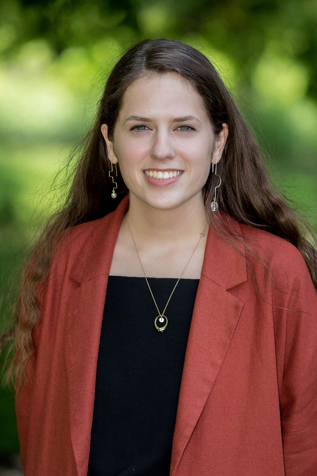 Portrait of a woman in a red blazer and black top, smiling outdoors. Ideal for professional bio or team page.