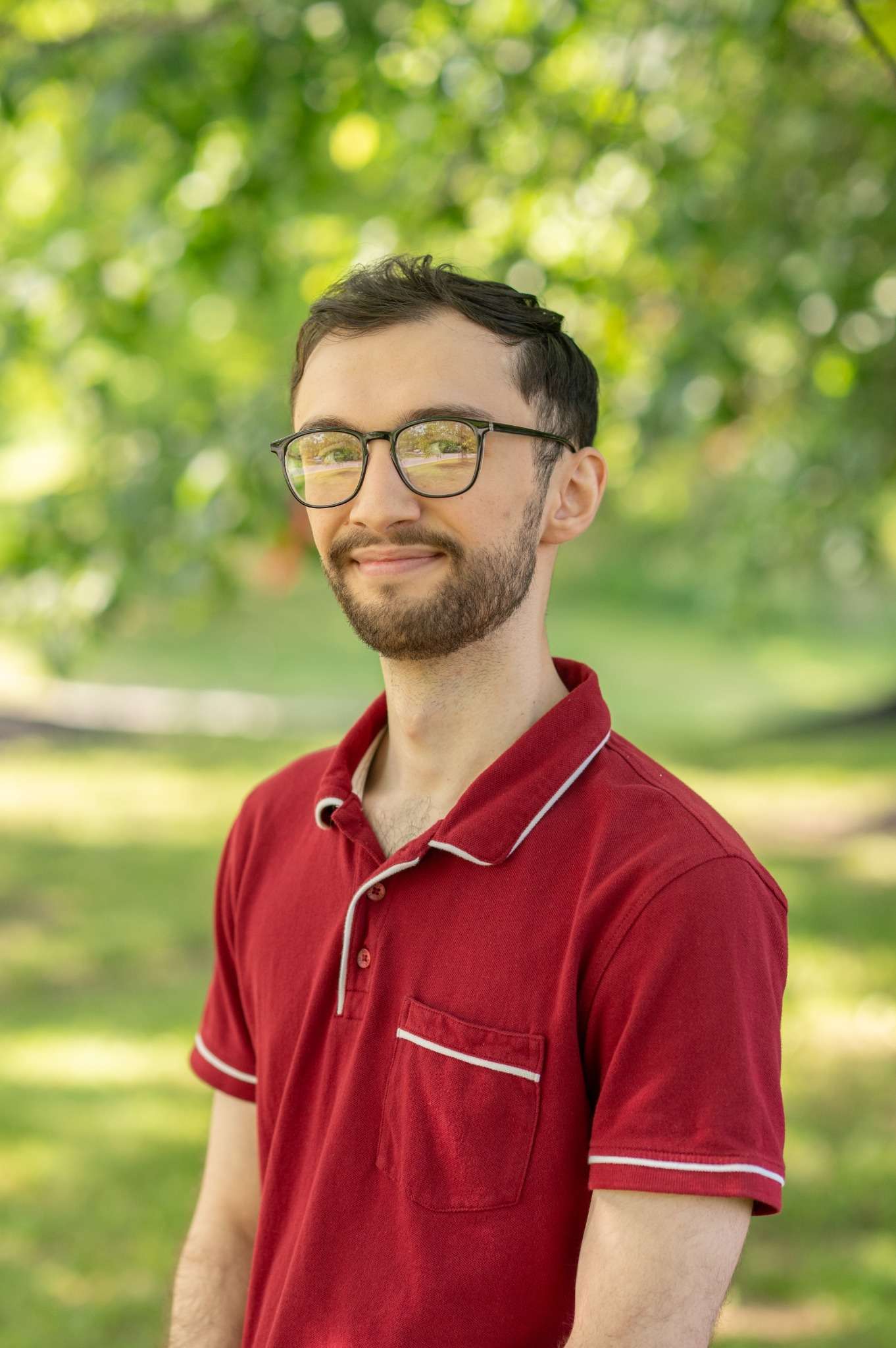 Professional headshot of man standing outdoors with a blurred green background.