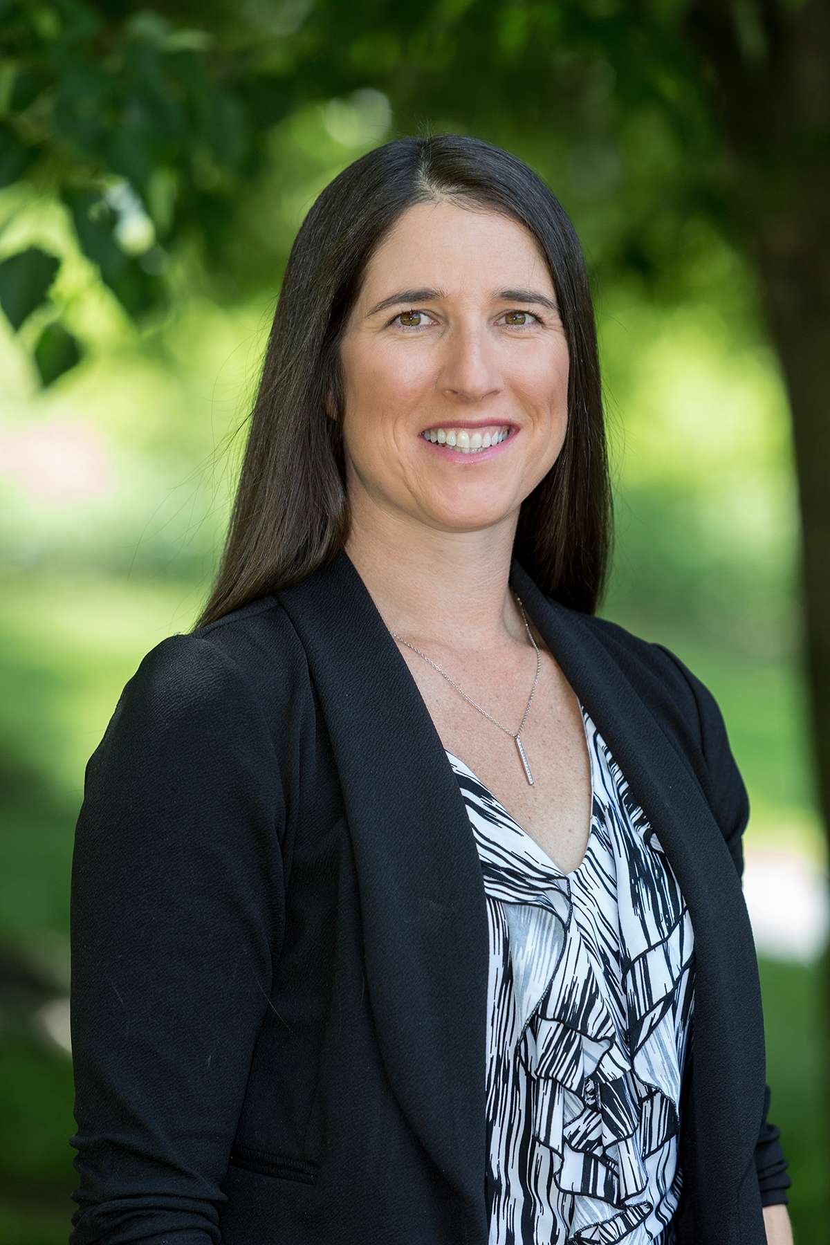 Professional headshot of woman standing outdoors with a blurred green background.
