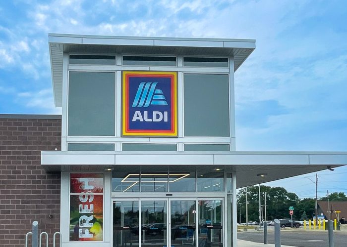 Exterior view of ALDI store entrance with fresh produce signage and clear blue sky.