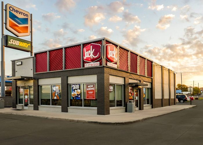 Jack in the Box fast food restaurant exterior at sunset with Chevron and Subway signs nearby.