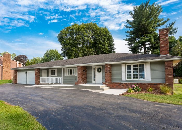 Single-story brick home with attached garage and a spacious driveway under a clear blue sky.