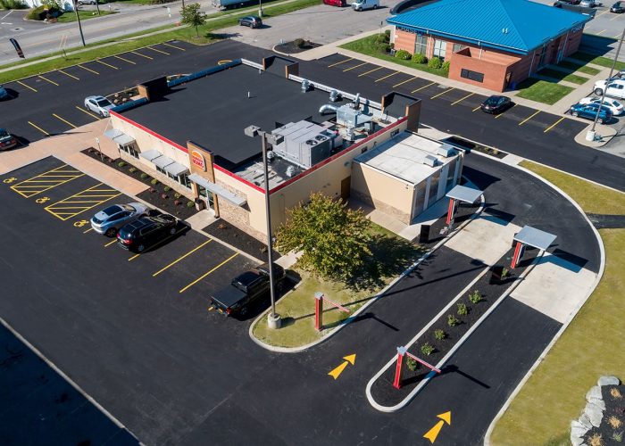 Aerial view of a fast-food restaurant with drive-thru and parking lot on a sunny day.