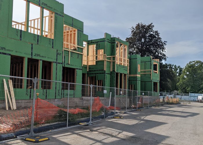 Construction of green residential building with wood framing and temporary fencing under a clear sky.