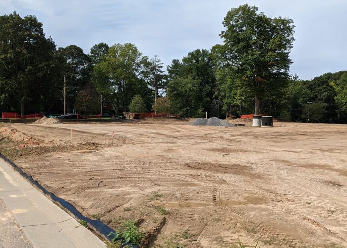 Construction site for new residential development with cleared land and trees in the background.