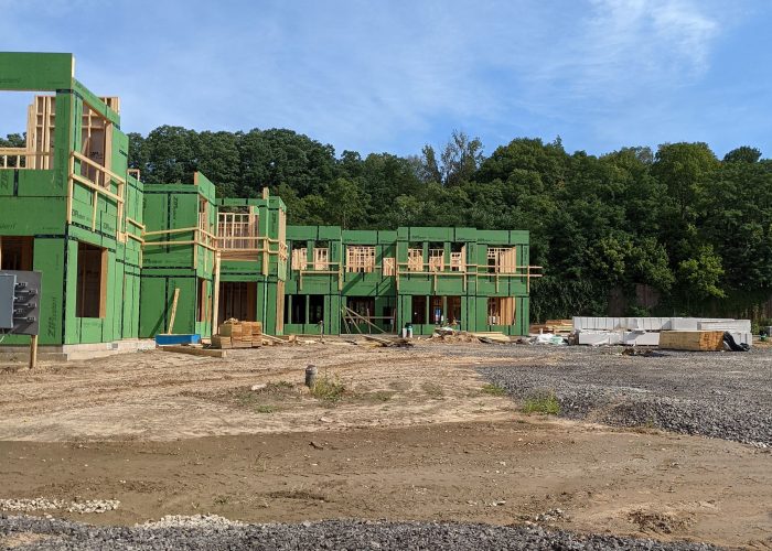 New housing development under construction with green sheathing and clear skies in background.